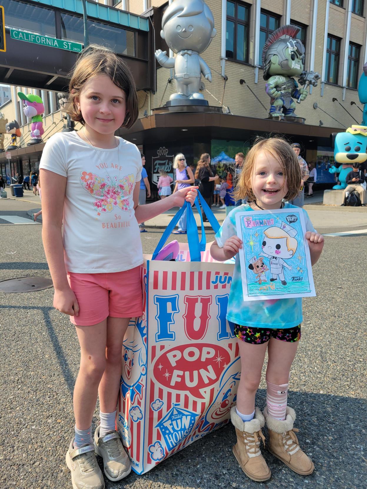 Children Enjoying the Day: Two children stand in front of the Funko Everett headquarters, holding a picture they’ve colored and a giant bag filled with goodies. In the background, you can see the sign for California Street, Funko statues on the outside of the building, and people lining up to go into the store.